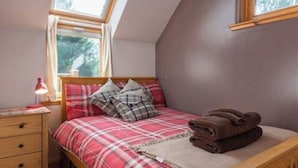 A bedroom with a sloped ceiling, a wooden bed frame, a red and white plaid bedspread, a bedside lamp, and a window with a view of trees. - The Beeches Studio - Highlands of Scotland (Newtonmore)