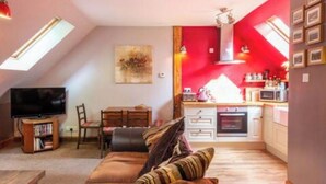 A cozy living room with a sofa and a television, a kitchen with red walls, and a dining area with a table and chairs. - The Beeches Studio - Highlands of Scotland (Newtonmore)