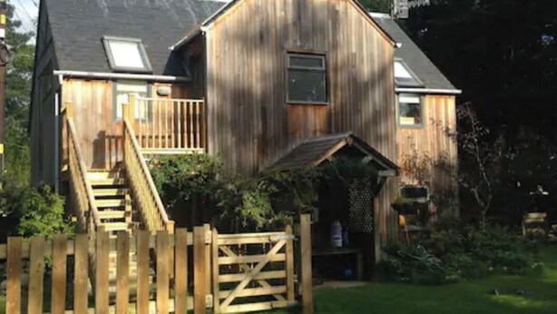 A wooden barn-style house with a front porch, a staircase leading to the entrance, and a wooden fence surrounding the property. - The Beeches Studio - Highlands of Scotland (Newtonmore)