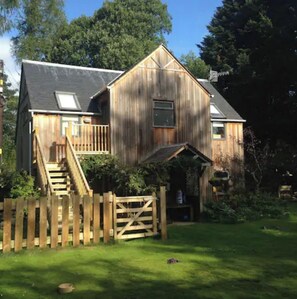 Ein hölzernes Bauernhaus mit Veranda und einer Treppe zum Eingang, umgeben von einem Holzzaun.