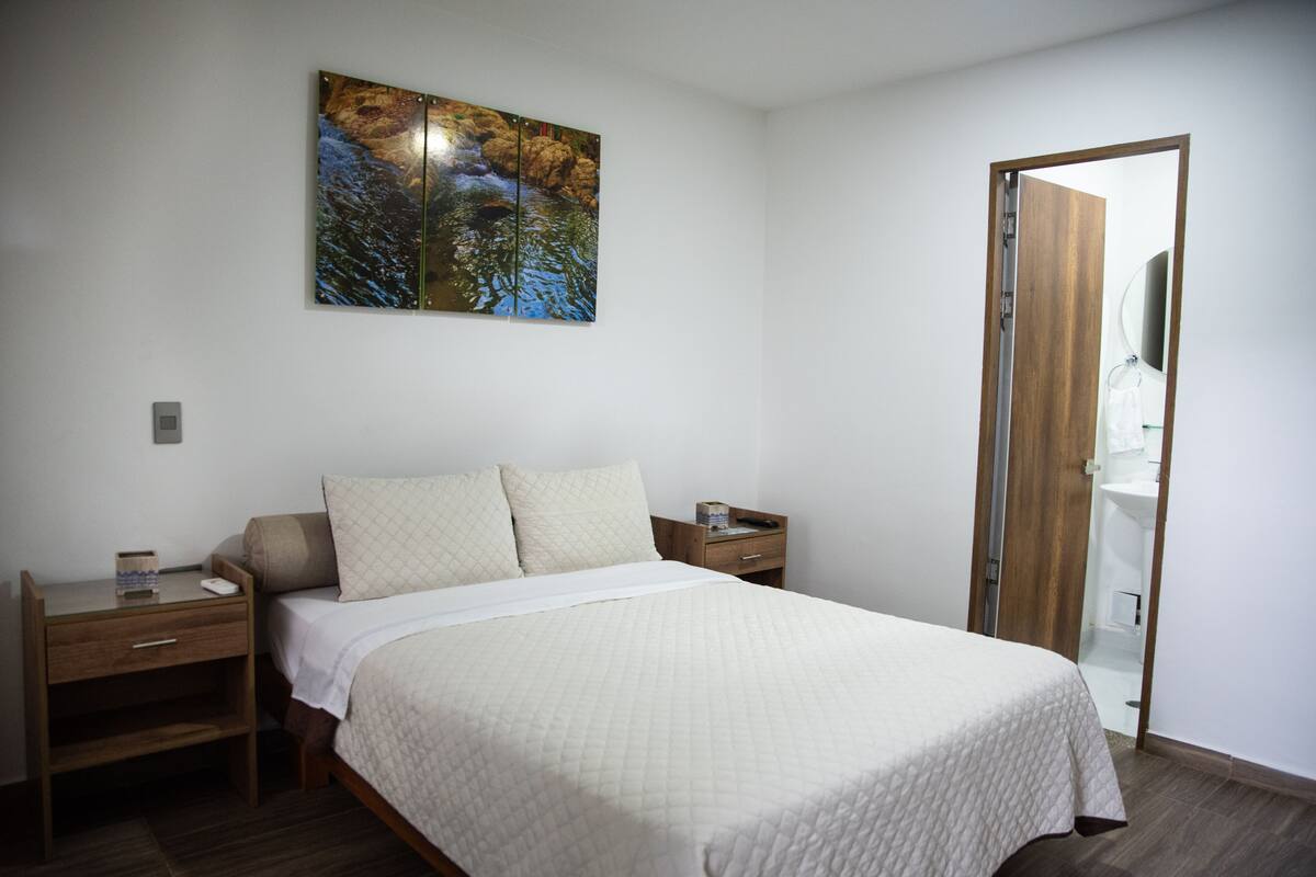 A bedroom with a bed, a nightstand, a bedside table, a mirror, and a painting on the wall.