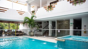 Une piscine intérieure à l’eau claire, avec un palmier et une vue sur l’intérieur du bâtiment.