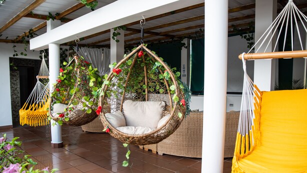 Un espace intérieur spacieux, agrémenté de fauteuils en osier suspendus et d’un fauteuil jaune, avec un sol carrelé et des piliers blancs.