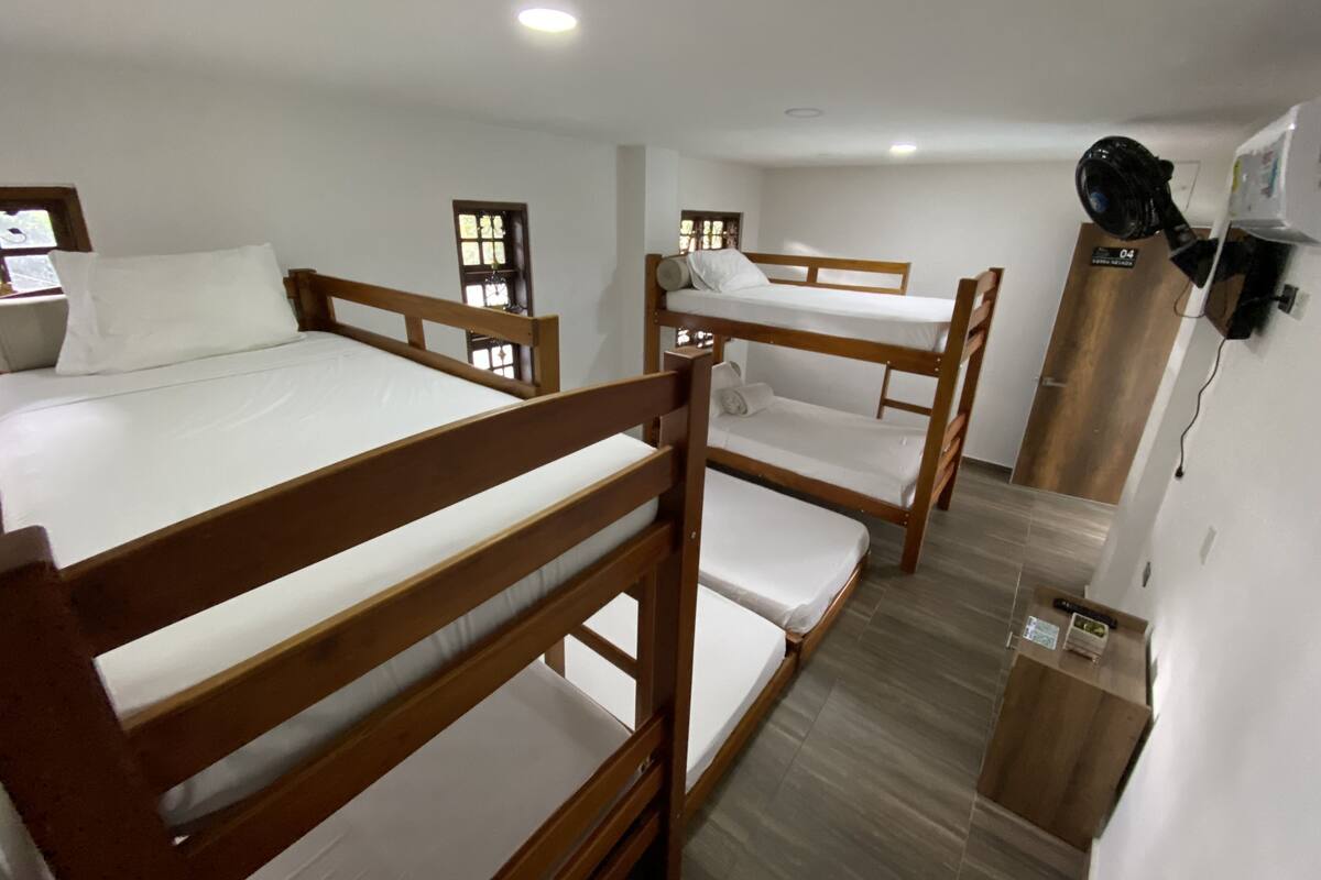 A room with three bunk beds, a wooden wardrobe, and a small desk with a chair.