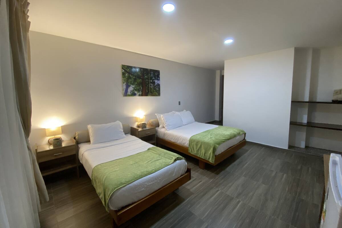 A hotel room with two beds, each with a nightstand and lamp, a painting on the wall, and a built-in shelf unit.