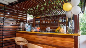 Un espace bar avec des lambris en bois, un comptoir orné de bouteilles, de verres et d’un ananas.