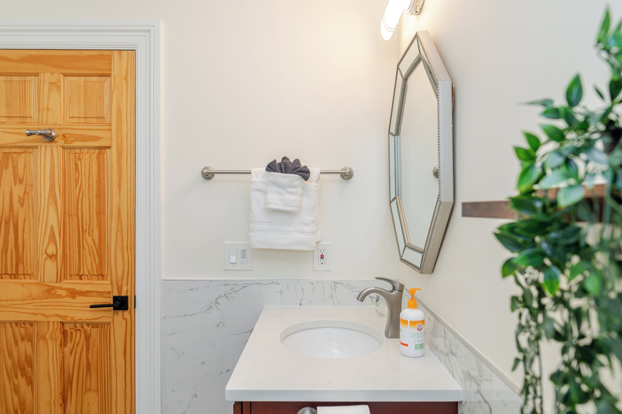 A bathroom with a wooden door, a white sink, a mirror, and a towel rack.