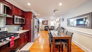 Una cocina moderna con electrodomésticos de acero inoxidable, armarios de madera y un comedor con una mesa grande y sillas.