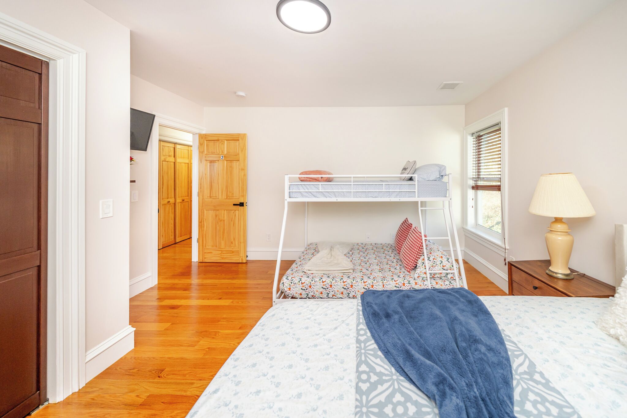 Un dormitorio con una cama litera, una mesita de noche con lámpara y una ventana con persianas.