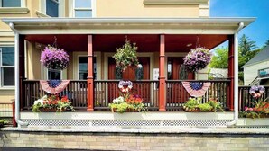 Una casa de dos pisos con un porche decorado con flores y banderas estadounidenses.
