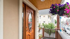 Una puerta de madera con un panel de vidrio, un balcón con barandilla y macetas colgantes de flores.