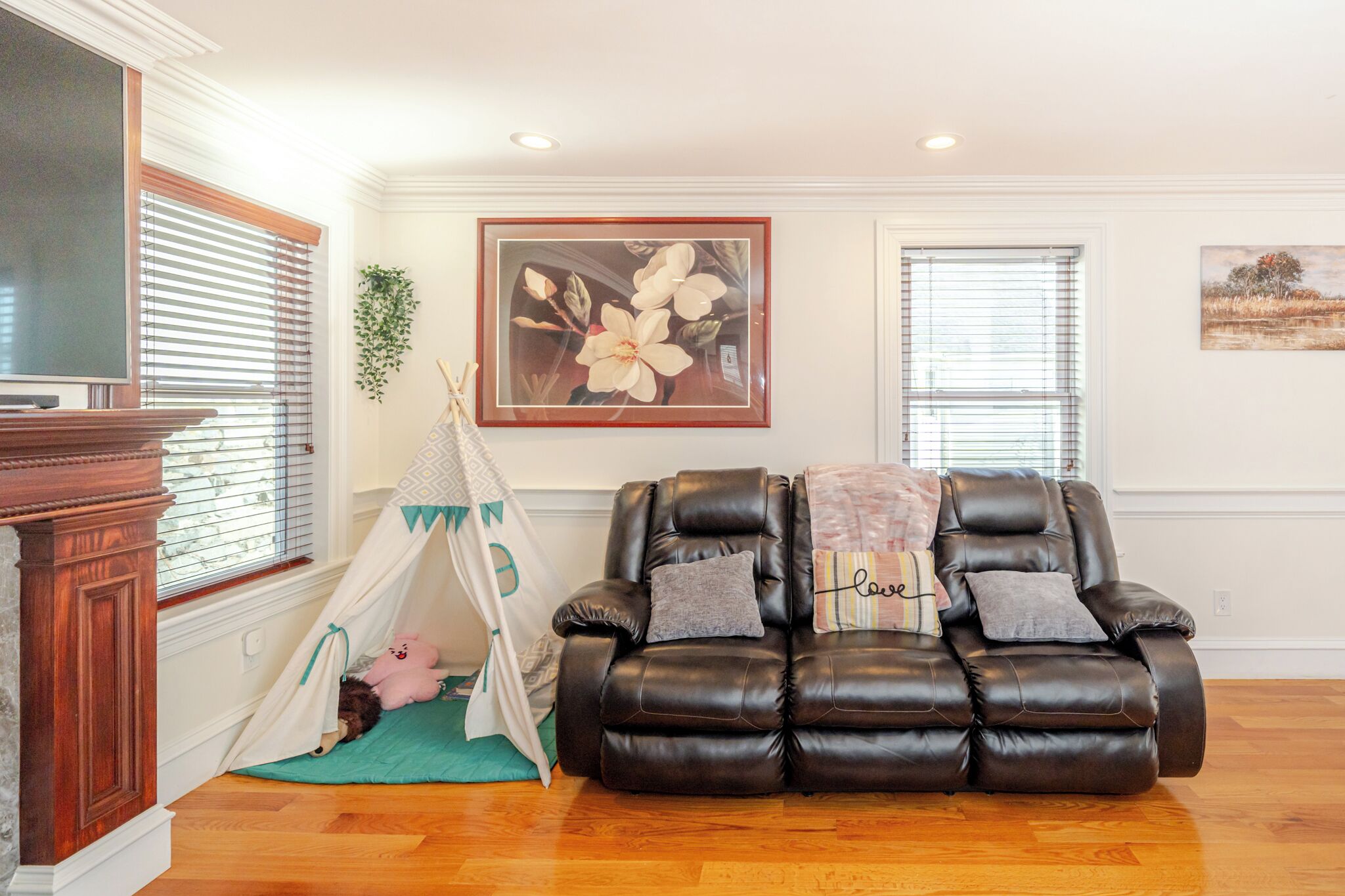 A living room with a brown leather sofa, a white tent, and a painting of flowers on the wall.