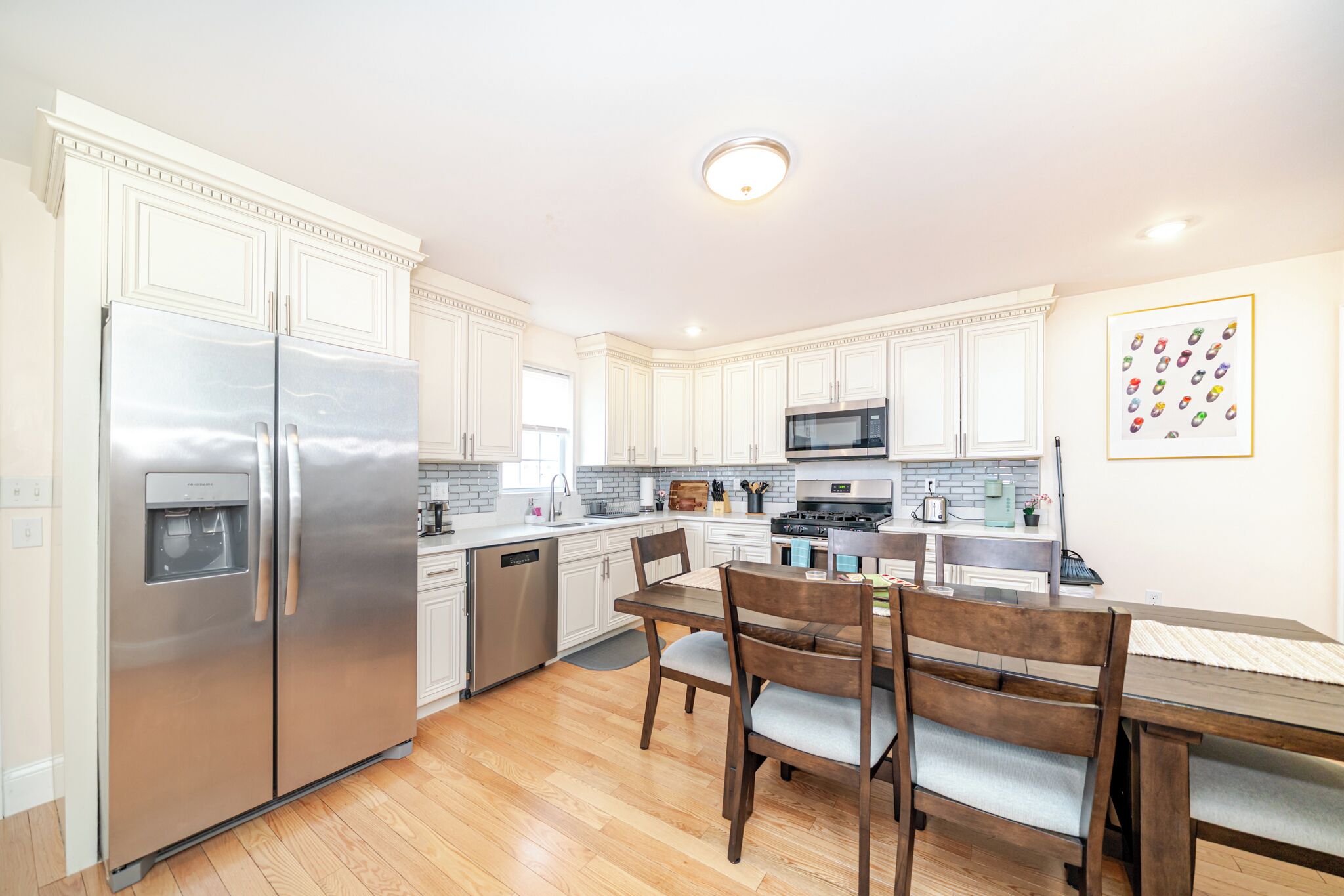 A modern kitchen with white cabinetry, stainless steel appliances, and a dining area with wooden furniture.