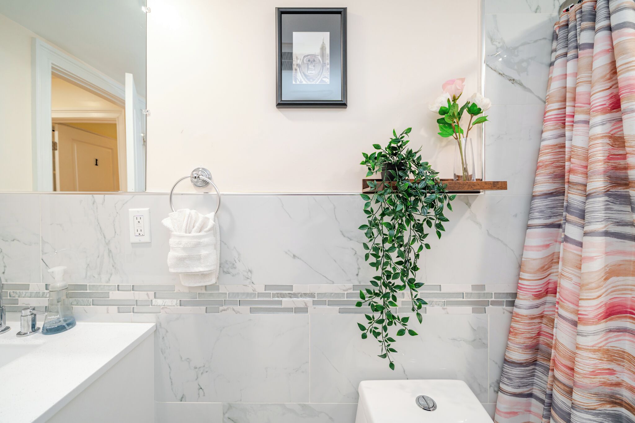 A bathroom with a marble sink, a toilet, a shower curtain, a framed picture on the wall, and a potted plant.