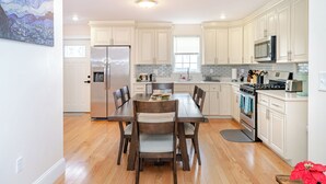 A modern kitchen with white cabinets, a stainless steel refrigerator, a dining table with chairs, and a microwave. - Newly Built Greater Boston Townhouse Near I-93 • Parking • Pet-Friendly - 39 (Quincy)
