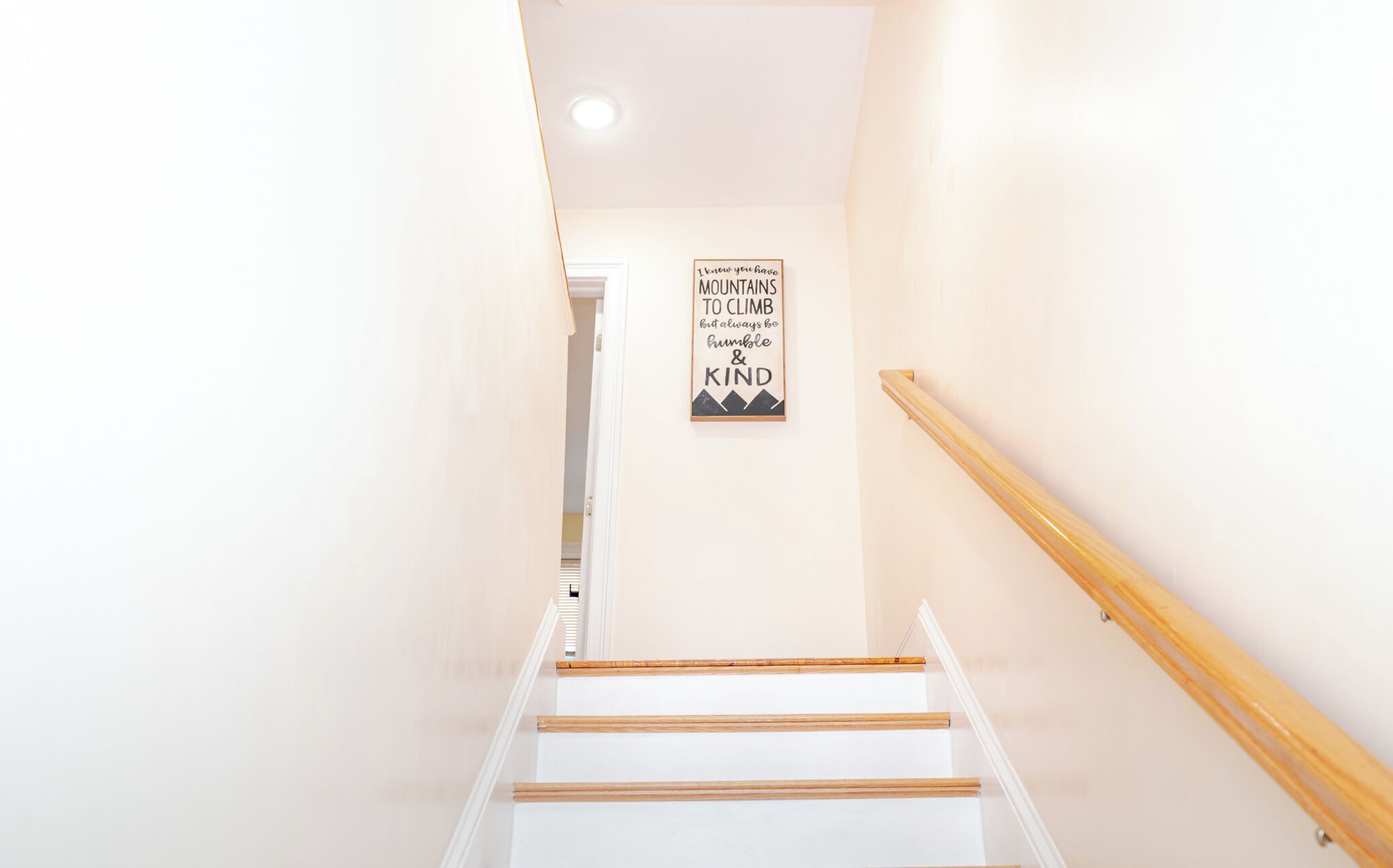 Eine Treppe mit hölzernen Geländern und einem an der Wand befestigten Schild, auf dem steht: „Ich kenne deine Basis. Berge zum Erklimmen, aber sei immer bescheiden und freundlich.“