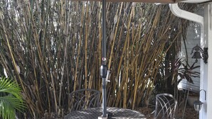 Ein runder Metalltisch mit Sonnenschirm, umgeben von Stühlen, auf einer Terrasse mit Bambus im Hintergrund.