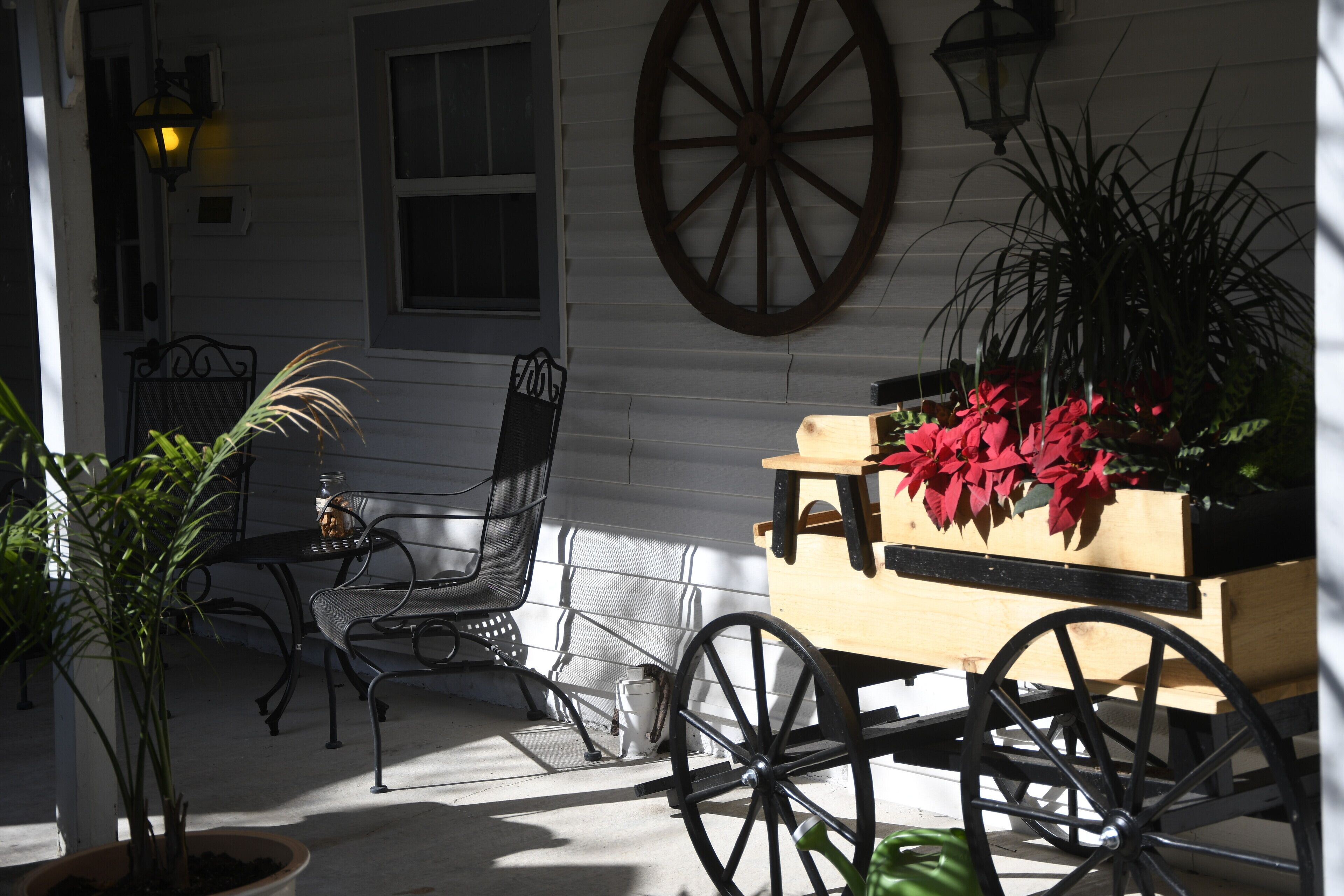 A porch with a wooden cart, a metal chair, and a potted plant.