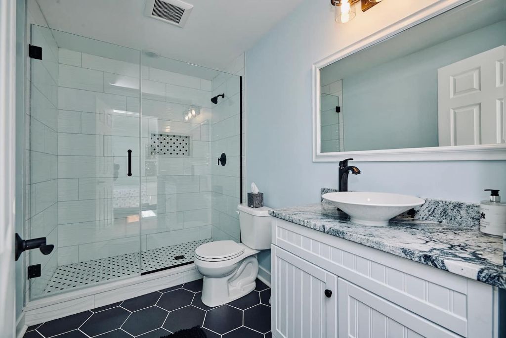 Un baño moderno con ducha de vidrio, inodoro blanco y encimera de mármol con lavamanos.