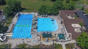 An aerial view of a swimming pool complex with multiple pools, a water slide, and surrounding buildings. - Fox Valley Farmhouse by the river - walk to town & pool (St. Charles)