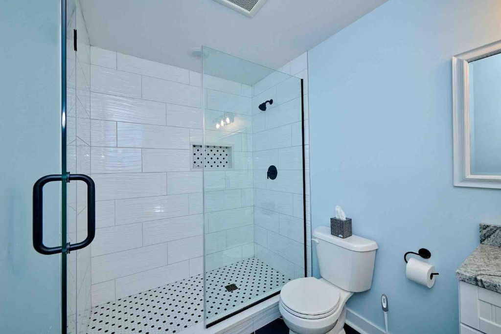 A bathroom with a glass-enclosed shower, white tiled walls, a toilet, and a sink with a granite countertop.