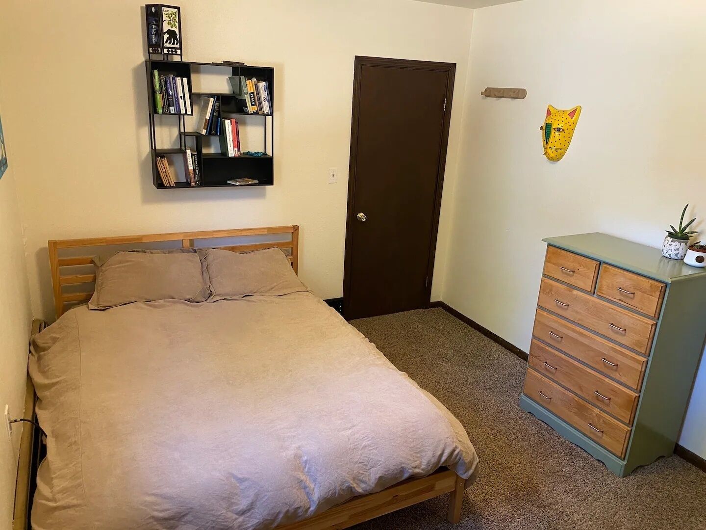 A bedroom with a bed, a bookshelf, a door, and a dresser.