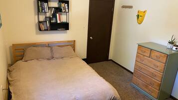 A bedroom with a bed, a bookshelf, a door, and a dresser.