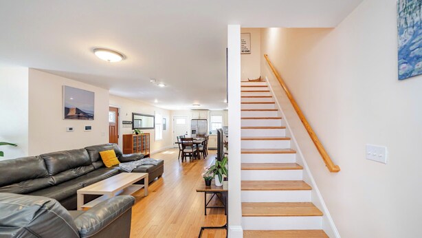 A spacious living room with a black leather sofa, wooden coffee table, and a staircase leading to an upper floor. - Spacious Greater Boston Townhouse Near I-93 • Parking • Pet-Friendly | 37 (Quincy)