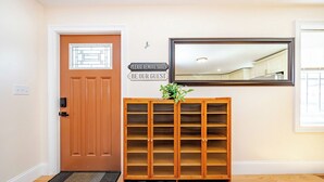 A wooden shoe rack with a sign above it, a door, and a mirror on the wall. - Spacious Greater Boston Townhouse Near I-93 • Parking • Pet-Friendly | 37 (Quincy)