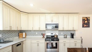 A modern kitchen with white cabinets, a stainless steel stove, and a microwave. - Spacious Greater Boston Townhouse Near I-93 • Parking • Pet-Friendly | 37 (Quincy)