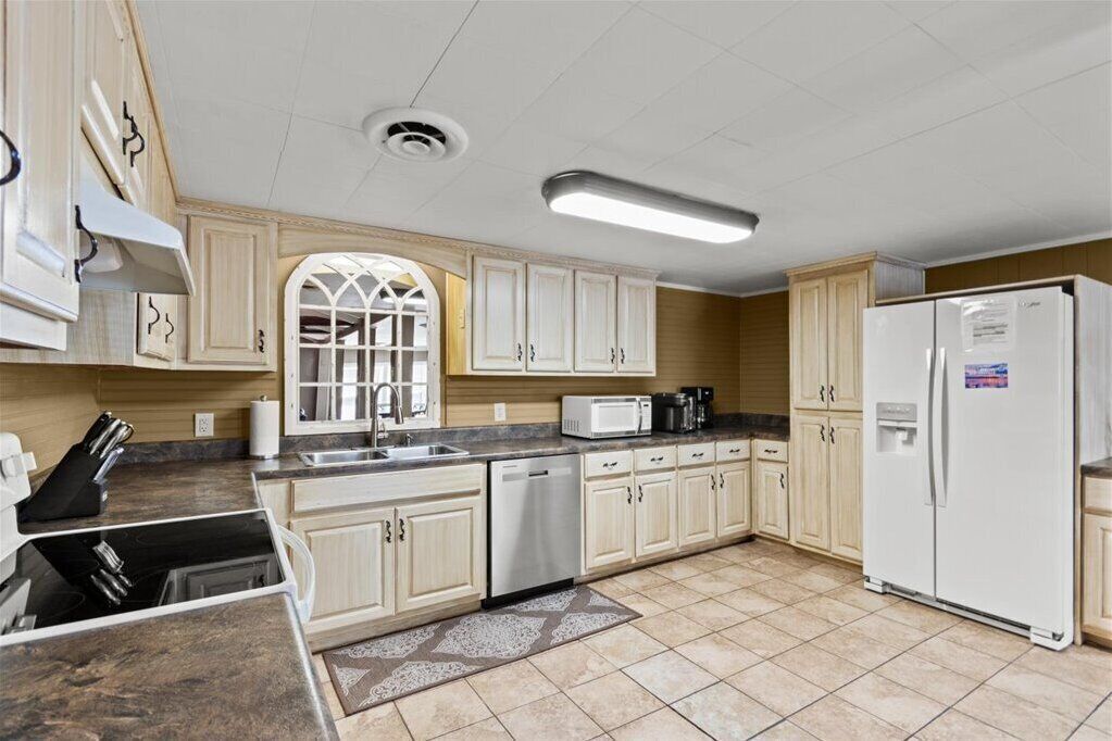 A kitchen with light wooden cabinets, a stainless steel dishwasher, a white refrigerator, and a microwave.