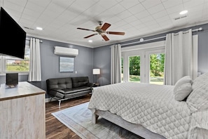 A bedroom with a bed, a ceiling fan, a desk, a chair, a TV, and a window with curtains.