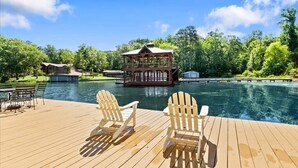 Une terrasse en bois avec des chaises Adirondack, une structure en bois construite au-dessus de l’eau et un ciel dégagé.