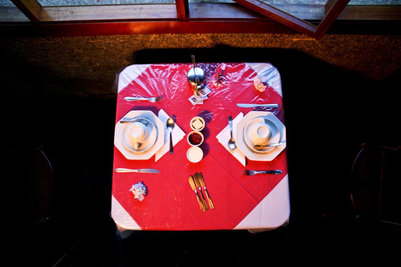 A dining table set with white plates, silverware, and a small bowl of condiments.