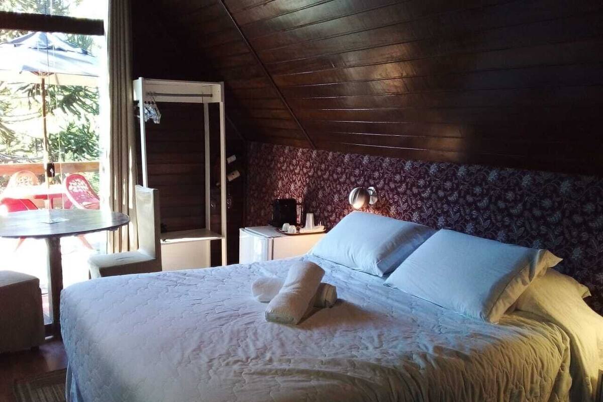 Ein Hotelzimmer mit Bett, einem kleinen Tisch, einem Stuhl und einem Fenster mit Blick auf Palmen.