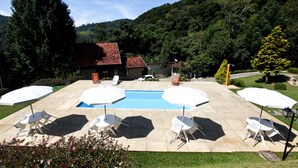 Un espace piscine agrémenté de parasols et de chaises blanches, entouré de verdure et avec une chaîne de montagnes en toile de fond.