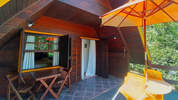 Une cabane en bois dotée d’un patio comprenant une table et des chaises, un parasol et une vue sur la verdure.