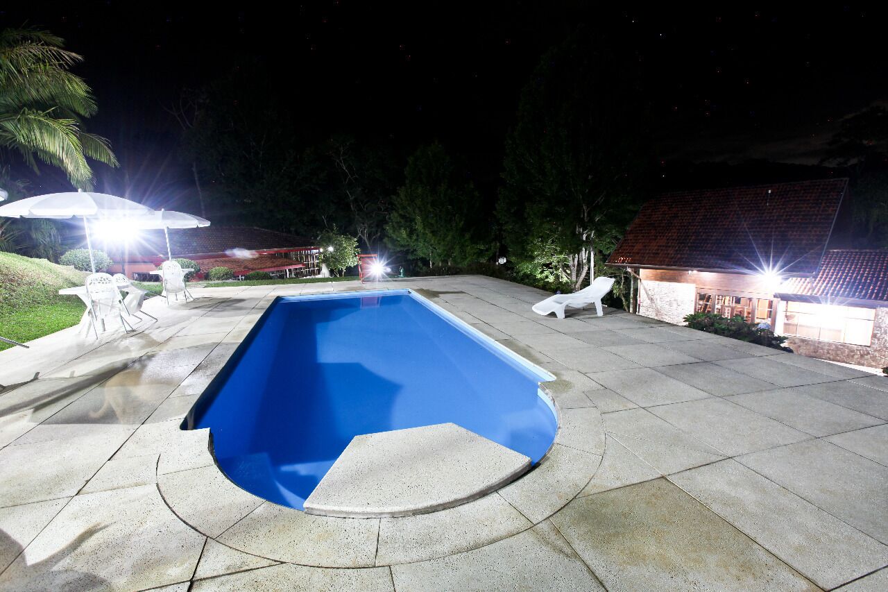 A swimming pool with a blue interior, surrounded by a paved patio area with outdoor furniture and umbrellas.