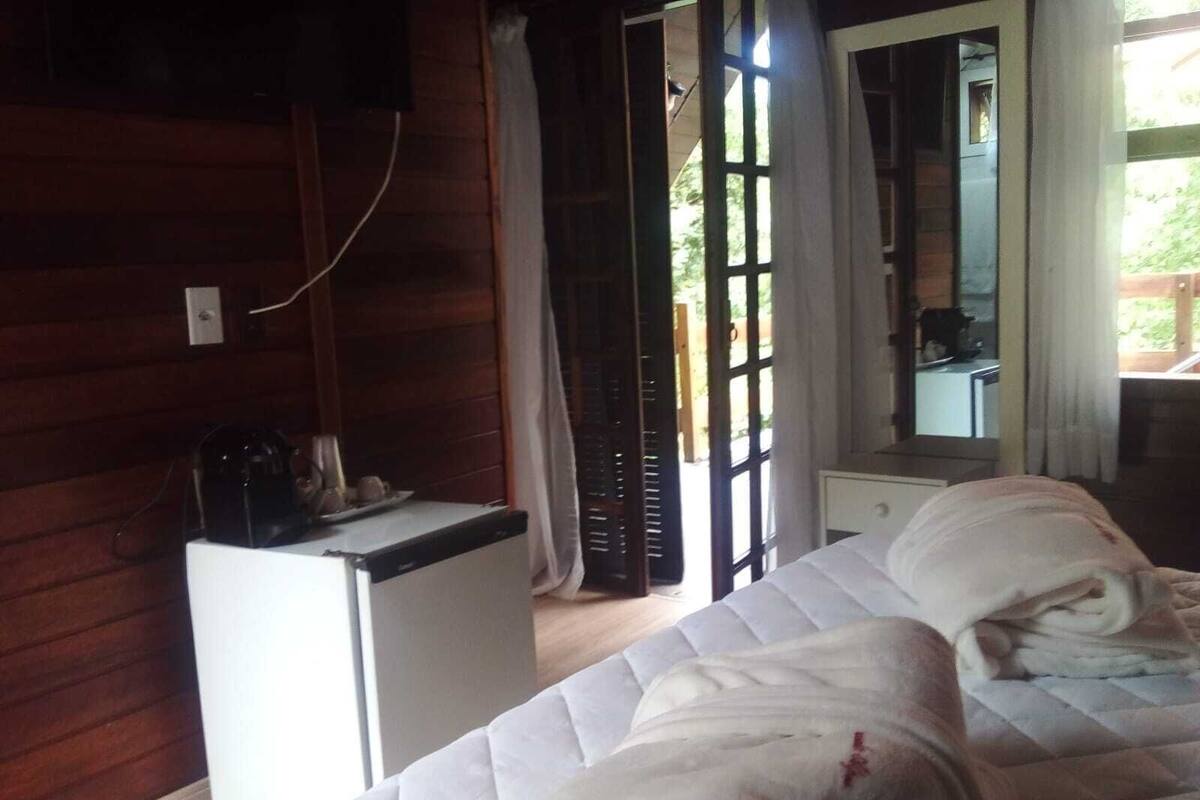 Ein Zimmer mit einem Bett, einem kleinen weißen Schreibtisch, einem Spiegel und einem Fenster mit Vorhängen.