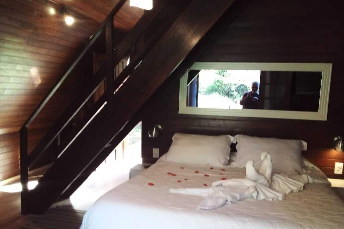 Ein Schlafzimmer mit einer Holztreppe, einem Bett mit weißen Leinen und einem Fenster mit Blick auf Grünflächen.