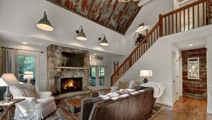 Amplio salón con chimenea de piedra, sofá de cuero y una escalera que conduce a un nivel superior.
