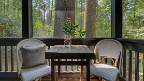 Una mesa de madera con dos sillas de mimbre en un porche con vistas a un bosque.