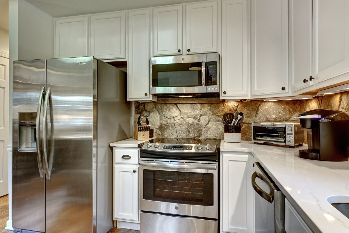 A kitchen with white cabinets, a stainless steel refrigerator, a microwave, a stove, and a toaster.
