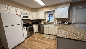 A modern kitchen with white cabinets, stainless steel appliances, and a granite countertop. - Witt's End at Mill Creek: Walk to Downtown | Creekside Retreat w/ Screened Porch (Highlands)
