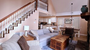 A spacious living room with a staircase, a dining area, and a kitchen in the background. - Witt's End at Mill Creek: Walk to Downtown | Creekside Retreat w/ Screened Porch (Highlands)