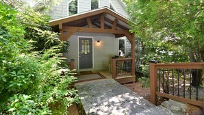A house with a covered porch, stone pathway, and wooden railing. - Witt's End at Mill Creek: Walk to Downtown | Creekside Retreat w/ Screened Porch (Highlands)