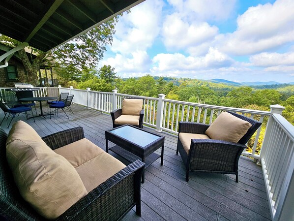 A deck with wicker furniture, a grill, and a scenic view of mountains.