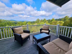 A deck with wicker furniture and a glass table, overlooking a forested landscape.