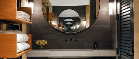 A modern bathroom with a large mirror, wooden shelves with towels, a sink, and a potted plant.