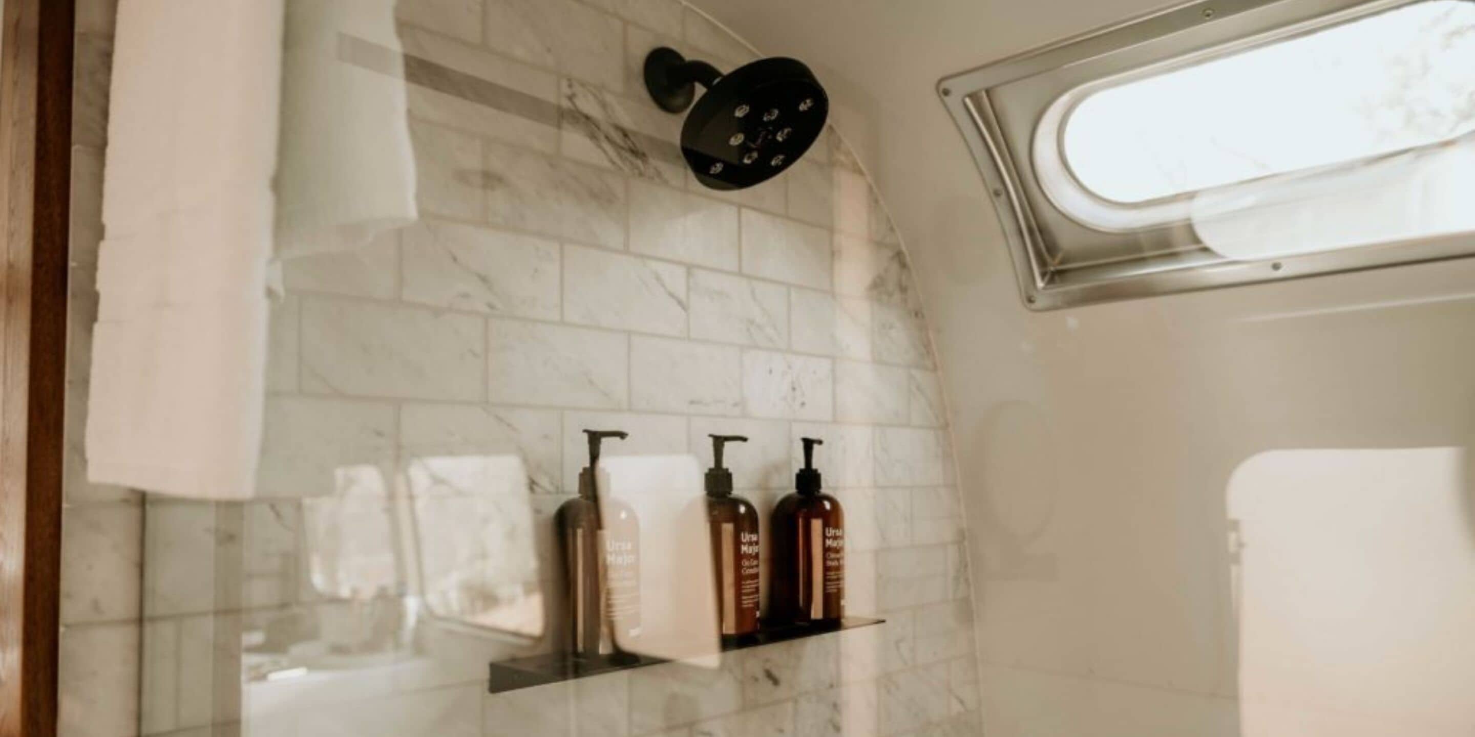 A bathroom with a shower, a window, and toiletries on a shelf.